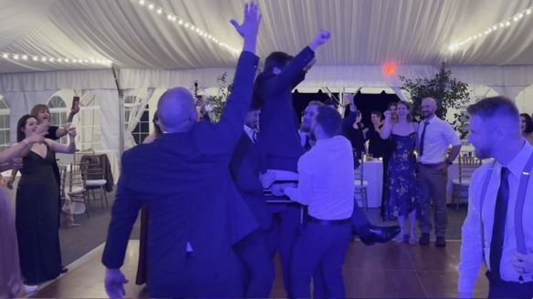 The crowd lifing the groom up on a chair.